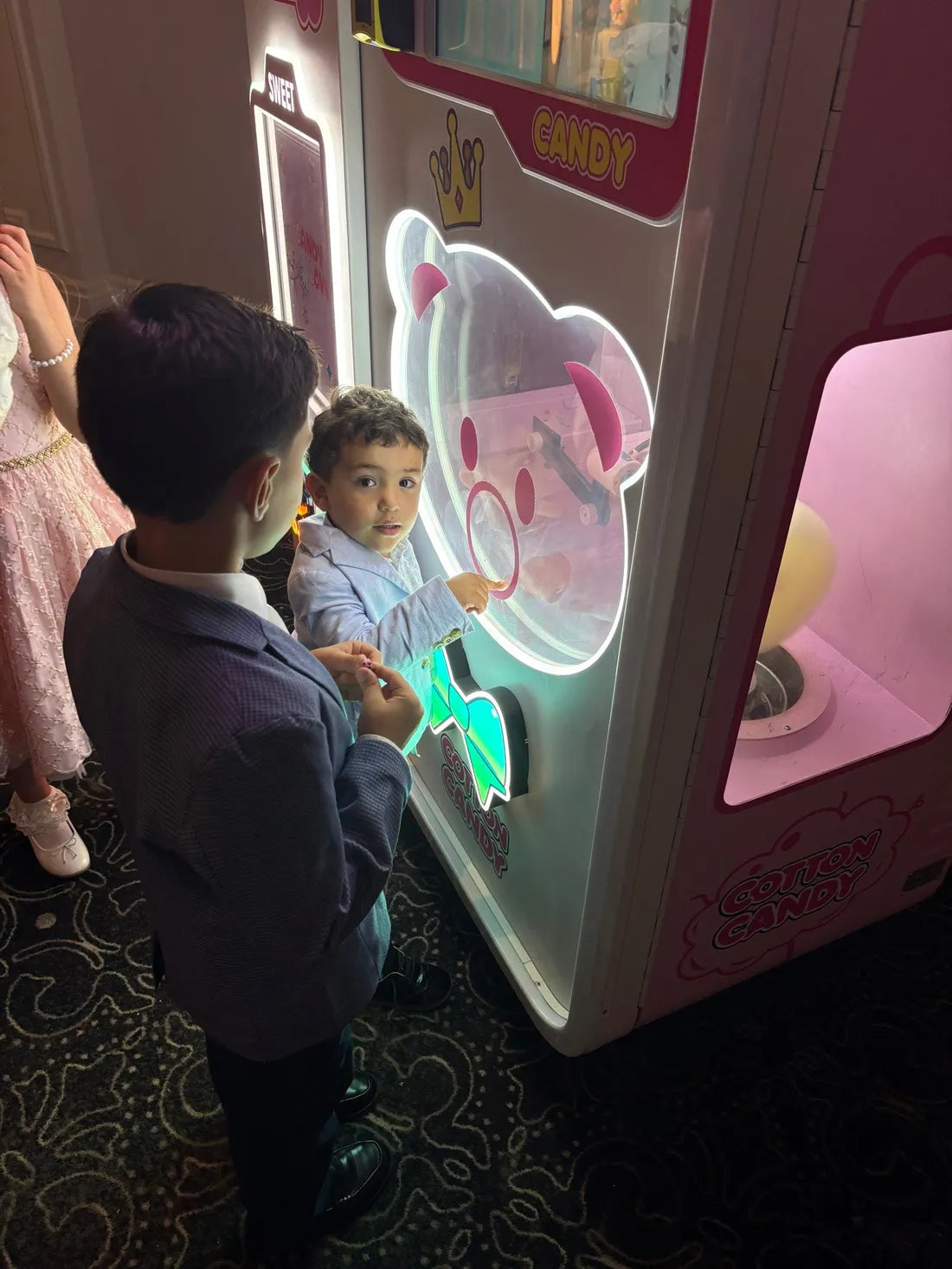 Two boys in dress clothes watch cotton candy spin inside the glowing bear machine at a party