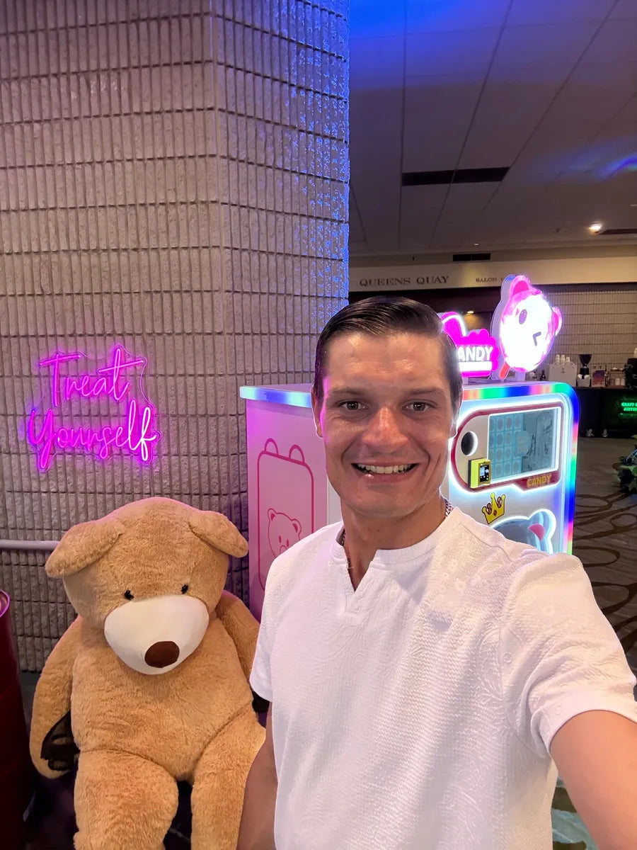A smiling Diligent host on site beside the lit machine and a giant teddy bear